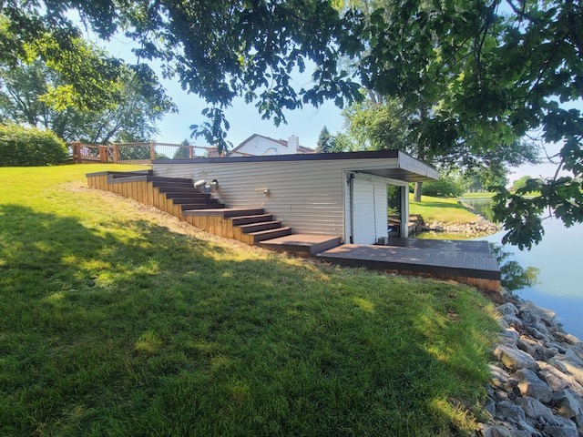 A modern lakeside retreat with steps leading down to a wooden deck by the water, surrounded by greenery.