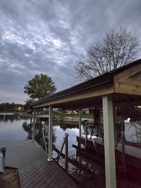 A serene waterfront scene showing a dock and a boat house under a cloudy sky, with trees in the background.