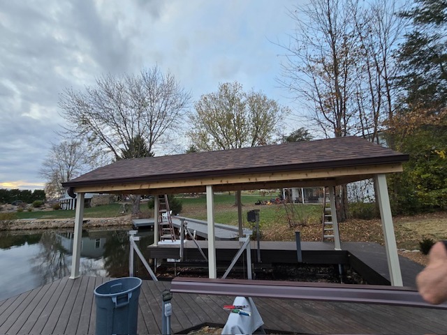 "Newly constructed dock with a covered boat slip near a calm waterway, surrounded by autumn trees and a cloudy sky."